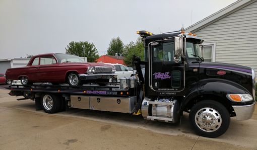 Black Larry Menz flatbed carrying a maroon classic car, purple door script